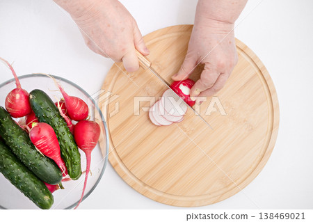 A woman's hands cutting radishes on a grey board 138469021
