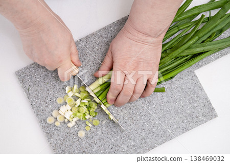Female hands cutting green onions on a grey board Female hands cutting green onions on a grey board 138469032