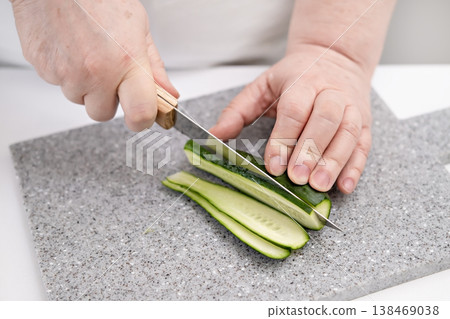 A woman's hands cutting a cucumber on a gray board A woman's hands cutting a cucumber on a gray board 138469038