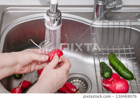 A woman's hands wash radishes under running water in the kitchen A woman's hands wash radishes under running water in the kitchen 138469076