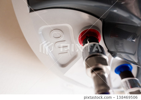 Close-up of a water heater connection with a metal valve and blue plastic cap. The heater is white with a visible label indicating the water inlet. Close-up of a water heater connection with a metal valve and blue plastic cap. The heater is white with a visible label indicating the water inlet. 138469506