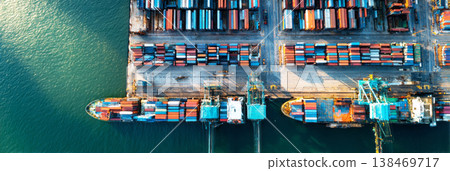 Containers are loaded and unloaded at the cargo sea port. Cranes move goods while large ships dock along the waterfront. Workers manage operations on the ships and wharf 138469717