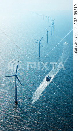 Rows of wind turbines stand tall and still in the sea, harnessing wind energy. The sun shines above and the water stretches far into the distance creating a clear view of the scene 138469719