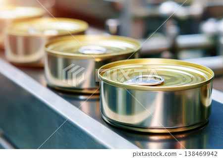 Cans move along the conveyor belt in a factory dedicated to canning food products. Workers oversee the machinery and ensure the production process runs smoothly in a busy setting 138469942
