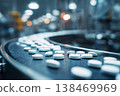 Tablets travel on a conveyor belt inside a pharmaceutical production facility. Workers monitor the process while machinery operates in the background 138469969
