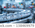 Numerous capped glass vials advance along a high-speed conveyor system on an automated pharmaceutical production line. This process takes place within a modern manufacturing plant 138469979