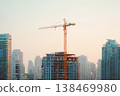 A tower crane stands tall above an unfinished high rise building. Other tall buildings surround the site. The scene shows an active construction area in a busy city during daylight 138469980