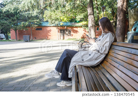 Beautiful woman using smartphone and sitting on bench outdoors Beautiful woman using smartphone and sitting on bench outdoors 138470545