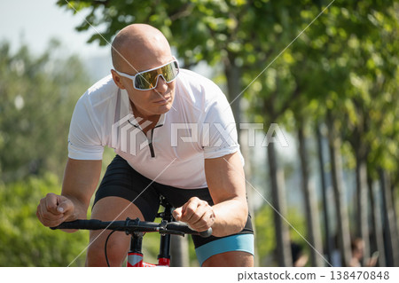 Athletic man riding road bicycle in park close up Athletic man riding road bicycle in park close up 138470848