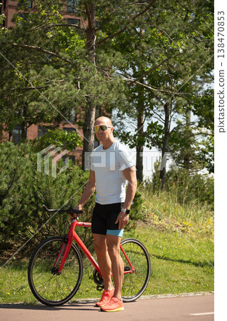 Athletic man standing with bicycle in park Athletic man standing with bicycle in park 138470853