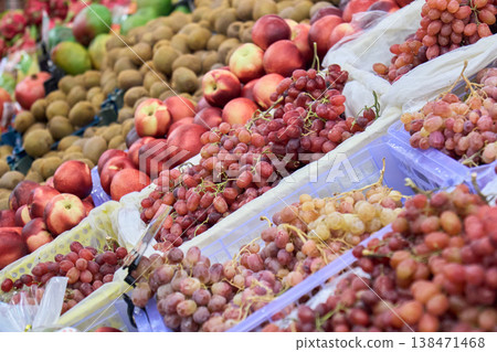 Fruit display at a market with various types of grapes, apples, and kiwis in the daytime 138471468