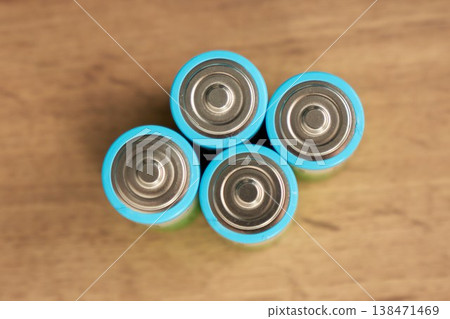 Four AA batteries are arranged in a square on a wooden surface 138471469