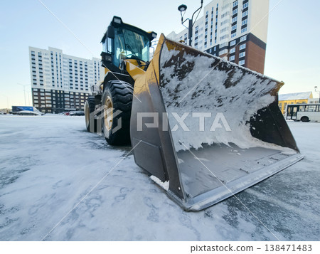 A large snow removal vehicle is working to clear snow from a parking lot next A large snow removal vehicle is working to clear snow from a parking lot next 138471483