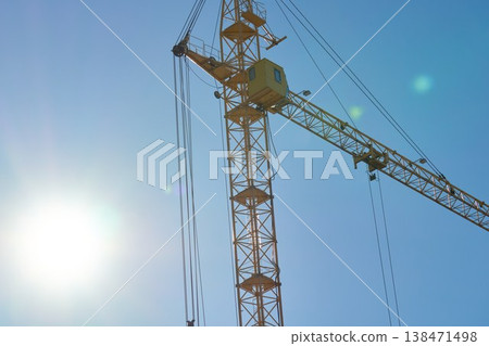 Construction crane stands tall against a clear sky during daytime work hours in an urban area with bright sunlight Construction crane stands tall against a clear sky during daytime work hours in an urban area with bright sunlight 138471498