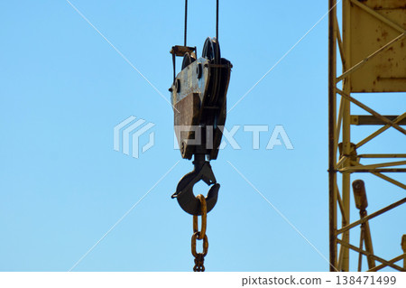 A construction crane stands tall at a building site. It lifts materials into the air while workers move around 138471499