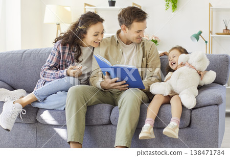 Happy family reading a storybook together on the sofa at home, playful moments Happy family reading a storybook together on the sofa at home, playful moments 138471784