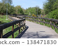 Wooden boardwalk with railing through green park landscape under clear sky. Outdoor pathway for walking, recreation, travel, nature exploration and peaceful environment in urban green zone. 138471830