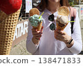 Woman holding two ice cream cones with different flavors and waffle biscuits outdoors. Summer dessert concept for street food, leisure lifestyle, travel moments and sweet refreshment. 138471833