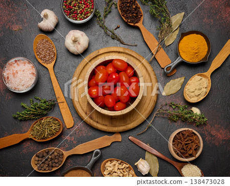 Cherry tomatoes in a wooden bowl and various spices on a dark table, top view 138473028