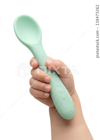 Toddler's small hand gripping a soft green silicone baby spoon, representing self-feeding practice, fine motor skills, and mealtime independence Toddler's small hand gripping a soft green silicone baby spoon, representing self-feeding practice, fine motor skills, and mealtime independence 138473262