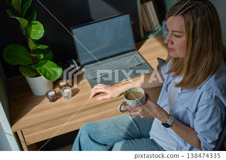 Woman holding mug while sitting at desk with laptop in home office, viewed from above 138474335