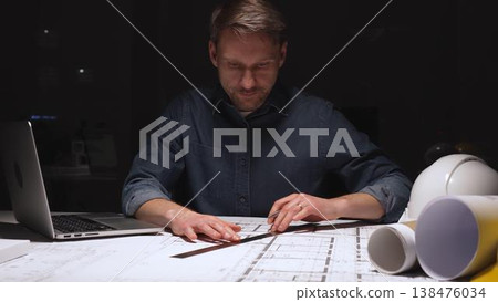 Architect working late into the night, focusing on detailed blueprints and construction plans using a ruler, illuminated by a focused spotlight on the desk 138476034
