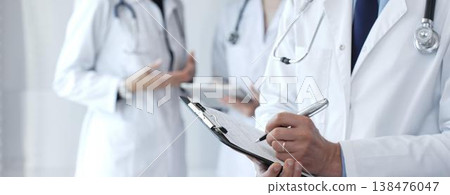 Doctor taking notes on clipboard during discussion with medical team involved in collaborative patient care, documentation, and health care strategy development in clinic 138476047