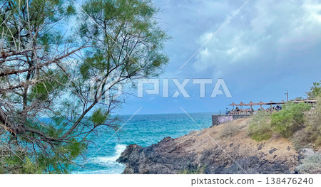 Rocky seaside coast with turquoise ocean, cloudy sky, trees and a terrace above the shore. Coastal travel, storm weather, scenic escape, seaside resort. Rocky seaside coast with turquoise ocean, cloudy sky, trees and a terrace above the shore. Coastal travel, storm weather, scenic escape, seaside resort. 138476240