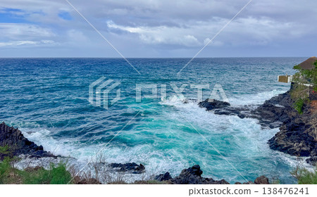 Turquoise ocean waves crash on black rocky coast under a cloudy sky. Dramatic seascape, coastal nature, storm weather, travel destination. Turquoise ocean waves crash on black rocky coast under a cloudy sky. Dramatic seascape, coastal nature, storm weather, travel destination. 138476241