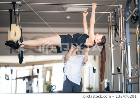 Pilates instructor assisting woman with advanced cadillac exercise Pilates instructor assisting woman with advanced cadillac exercise 138476291