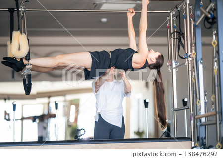 Woman practicing advanced pilates exercise with instructor assisting Woman practicing advanced pilates exercise with instructor assisting 138476292