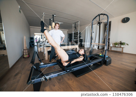 Woman exercising pilates reformer with personal instructor training Woman exercising pilates reformer with personal instructor training 138476306