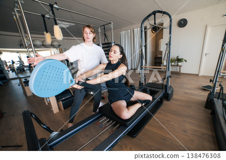 Woman performing pilates exercise with trainer on reformer 138476308