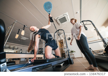 Woman exercising pilates cadillac with instructor guidance Woman exercising pilates cadillac with instructor guidance 138476317