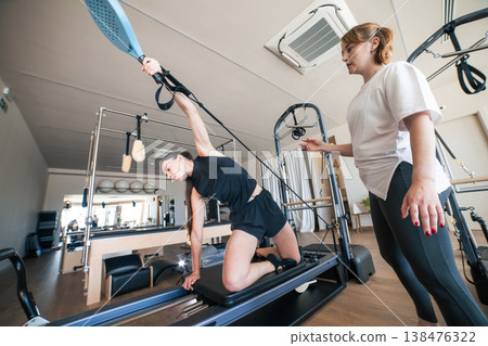 Woman exercising on pilates reformer with instructor 138476322