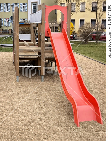 A bright red plastic slide on an empty playground in the city 138477180