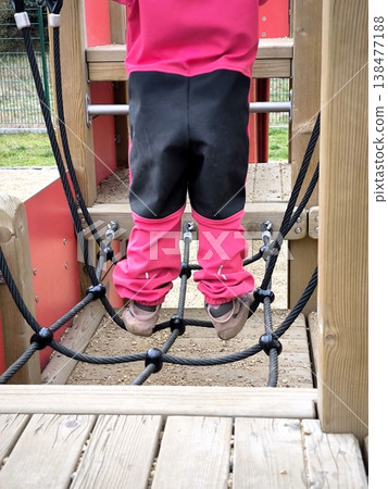 A child in a pink suit moves along a rope net at a playground A child in a pink suit moves along a rope net at a playground 138477188