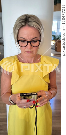 Blonde in yellow dress looks intently at smartphone Blonde in yellow dress looks intently at smartphone 138477215