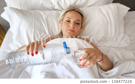 Blonde lying in bed drinking water in the morning 138477228