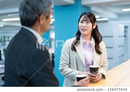 Office workers, a man and a woman, chatting while drinking coffee in the office. Office workers, a man and a woman, chatting while drinking coffee in the office. 138477434