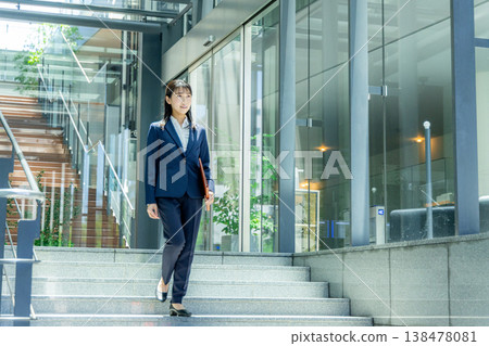 一位身穿西裝的年輕女子走進辦公大樓入口。 138478081