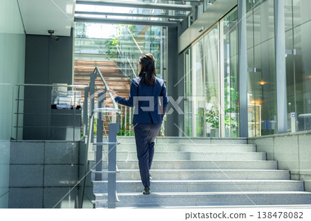 A young woman in a suit walking through the entrance of an office building. 138478082