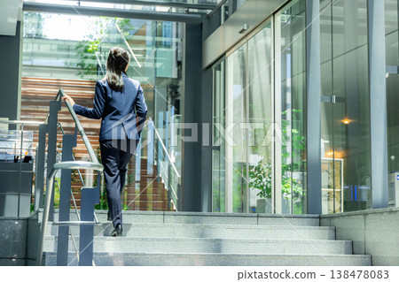 A young woman in a suit walking through the entrance of an office building. 138478083
