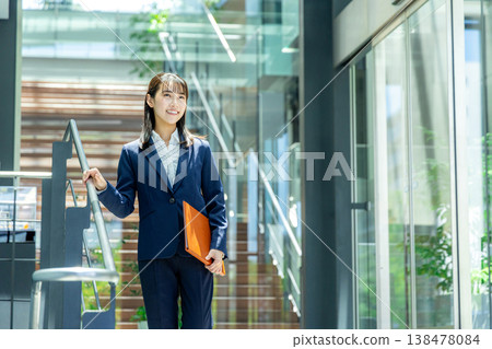 一位身穿西裝的年輕女子走進辦公大樓入口。 138478084