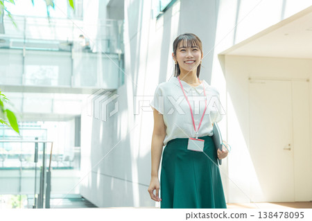 一位年輕女子手裡拿著筆記本，走在走廊上。 138478095