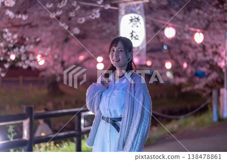 一位二十多歲的女子身穿開襟羊毛衫,漫步在著名的賞櫻勝地。燈光璀璨的櫻花和燈籠營造出濃厚的旅遊氛圍。 一位二十多歲的女子身穿開襟羊毛衫,漫步在著名的賞櫻勝地。燈光璀璨的櫻花和燈籠營造出濃厚的旅遊氛圍。 138478861