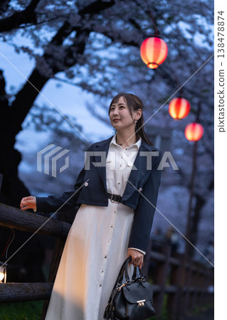 一位二十多歲的女子漫步在著名的賞櫻勝地;夜晚,櫻花和燈籠在燈光的映襯下熠熠生輝;這是一幅遊客的畫面。 一位二十多歲的女子漫步在著名的賞櫻勝地;夜晚,櫻花和燈籠在燈光的映襯下熠熠生輝;這是一幅遊客的畫面。 138478874