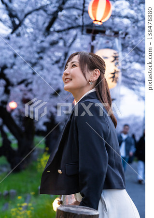 A woman in her 20s strolling through a famous cherry blossom viewing spot; illuminated cherry blossoms and lanterns at night; a tourist image. A woman in her 20s strolling through a famous cherry blossom viewing spot; illuminated cherry blossoms and lanterns at night; a tourist image. 138478880