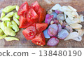 A vibrant assortment of fresh, raw cooking ingredients including chopped tomatoes, shallots, garlic cloves, and green chilies, neatly arranged on a wooden cutting board, ready for meal preparation. 138480190