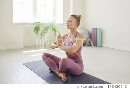 Yogi fit woman sitting on yoga mat in lotus pose, meditating calmly, holding hands together Yogi fit woman sitting on yoga mat in lotus pose, meditating calmly, holding hands together 138480342